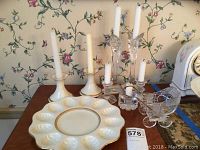 Overview of Lenox egg dish, candle holders, glass candlesticks, and glass baby carriage on wooden table with floral wallpaper background