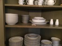 Shelves holding stacks of plates, bowls, cups, and serving pieces arranged orderly for display.