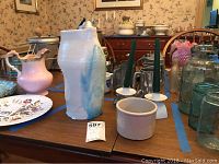 Wide view of Roseville crock, pink ceramic pitcher, candlesticks, glass jars and other items on table