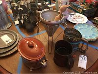 Full table display of vintage kitchen items including sifters, chinoises strainer, ceramic baking dish, mugs and plates.