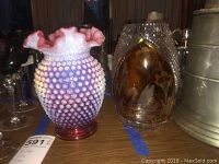 Two glass vases side by side on table, one pink and white hobnail ruffled top vase, other amber glass vase with etched swan design.