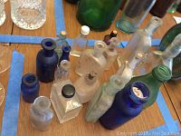Various antique and vintage bottles in different colors and shapes, some with corks, arranged on wooden surface