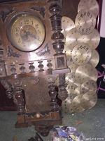 Ornate antique wooden clock case with clock face and multiple separate clock faces on a wooden plank next to it.