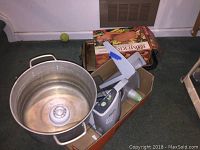 Photo of large metal stock pot and assorted kitchen items including boxed cookware.