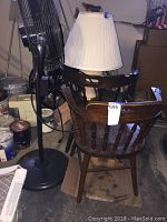 Two vintage wooden chairs with visible wear, floor fan and lamp grouped together