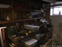 Wooden workbench with various hand tools, small boxes, tapes, and other hardware items on top and below shelves in a workshop room with window.