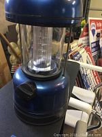Close-up of a blue iZoom LED mini lantern with on/off knob and transparent plastic casing.