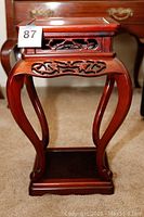 Front view of rosewood end table showing curved legs, intricate carvings on apron and sides, and lower shelf base.