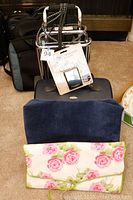 Folding luggage rack, navy blue back cushion, hanging rose floral toiletry bag, and Samsonite jewelry tote in background.