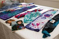 Table with multiple scarves laid out in a row including rectangular printed scarves, an infinity scarf, and two books about scarf tying.