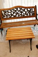 Wrought iron bench with wooden slats and floral backrest alongside matching wooden slat topped table