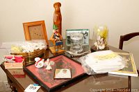 Wide view of lot items on table showing frames, figurines, glass dome, linens, and small collectibles