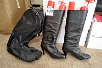 Front side view of the pair of black women's boots with suede insets beside a black boot bag. Boots are next to each other with boot shapers inside.