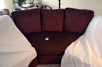 Front view of the burgundy curved wedge couch with three loose back cushions.