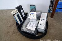 Lot items arranged in a round black fabric case on carpet, showing retail boxes for Fitbit Flex, power bank, flashlight, and tablet cover with tag indicating Galaxy tablet
