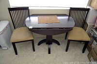 The drop leaf table with both leaves down showing the narrow form with two beige cushioned seat chairs beside it.