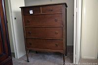 Front view of wooden chest of drawers showing five drawers and turned legs with rollers.