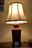 Front view of oxblood porcelain vase lamp with cream fabric lamp shade illuminated