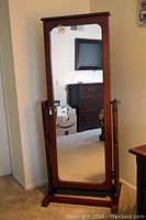 Full-length view of the cherry wood jewelry armoire with cheval mirror tilted upright, showing its height and sturdy wooden frame.