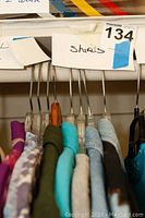 Photo showing multiple women's shirts hanging on hangers labeled 'Shirts'.