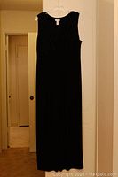 Solid black sleeveless ankle-length dress hanging on hanger against closed door.