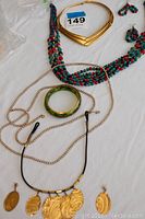 Four necklaces along with a green bangle bracelet and a pair of gold-tone earrings arranged on a surface.
