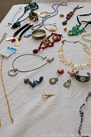 Photo showing various necklaces, bracelets, and earrings laid on a white surface, displaying the assortment and styles.