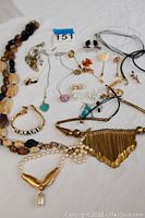 Photo displays assortment of costume jewelry items on white surface including necklaces, bracelet, earrings, and pins.