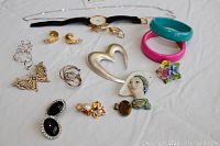 Full view of all costume jewelry pieces including bracelets, pins, earrings, watch, pendant, and chain laid out on white surface.