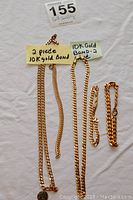Five gold-tone chains laid side by side on white background with lot number and sticky labels