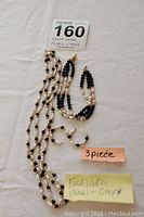 Photo showing the fresh water pearl and black onyx necklace, bracelet, and pierced earrings with maxsold lot tag and notes.