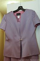 Front view of lilac short sleeve jacket with jewel closure hanging on hanger