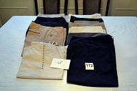 Top view of 11 pairs of women's pants arranged folded on a bed, showing variety of colors and button details on some pants.