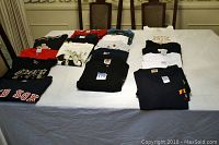 Full table view of a variety of men's and women's t-shirts and sweatshirts laid out flat, showing different colors and prints.