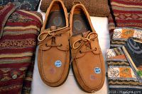 Pair of new light brown Bass moccasin-style shoes with laces, marked size 10M, placed on a colorful shirt background.