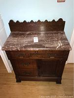 Front view of antique wash sink showing marble top, wooden base with three drawers and one cabinet door, ornate carved backsplash, and metal handles.