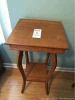 Front view of wooden side table showing square top and curved legs with lower shelf.