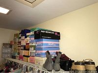 Stacked shoe boxes on closet shelf with some pairs of shoes visible including grey suede boots and black heels