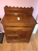 Front view of antique wooden wash sink cabinet with decorative backboard and metal drawer pulls.