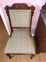 Front view of the antique wooden side chair showing carved backrest and patterned upholstery on seat and backrest.