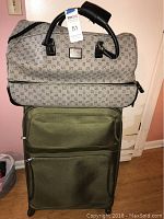 Photo of two bags stacked: a green rolling suitcase below and a beige patterned duffel bag on top.