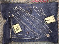 Photo showing multiple sterling silver necklaces, bracelet, and two sets of earrings arranged on a dark towel.