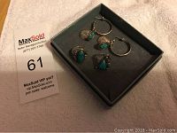 Silver rings and turquoise stone hoop earrings in black jewelry box on beige background