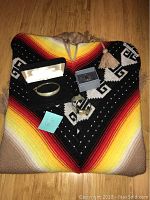 Full view of the poncho spread out on the floor with the bracelet, cuff bracelet, and earring box displayed on top.
