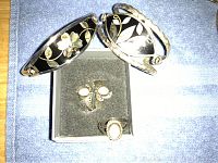 Two silver-tone bracelets with black floral and leaf inlay designs, silver-tone ring with cream-colored oval stone, and matching clip-on earrings with cream stones.