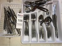 Photo of silverware and airline knives organized in trays and a basket, showing forks, spoons, knives, and serving utensils.