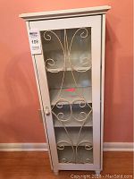 Front view of the white display cabinet showing the glass door with metal scrollwork design.