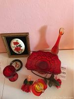Photo showing the tall red and yellow glass decanter, red glass bowl, red goblet, framed floral art piece, small decorative plate, floral and pumpkin decorations, and a small figurine.