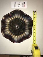 Overhead photo of the carnival glass dish showing scalloped edges and radiant pattern, tape measure alongside showing about 7.5 inches size.