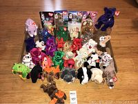 Wide shot of all the Ty Beanie Babies arranged together on a wooden floor, showing a variety of colors and animal types with Ty tags mostly attached.